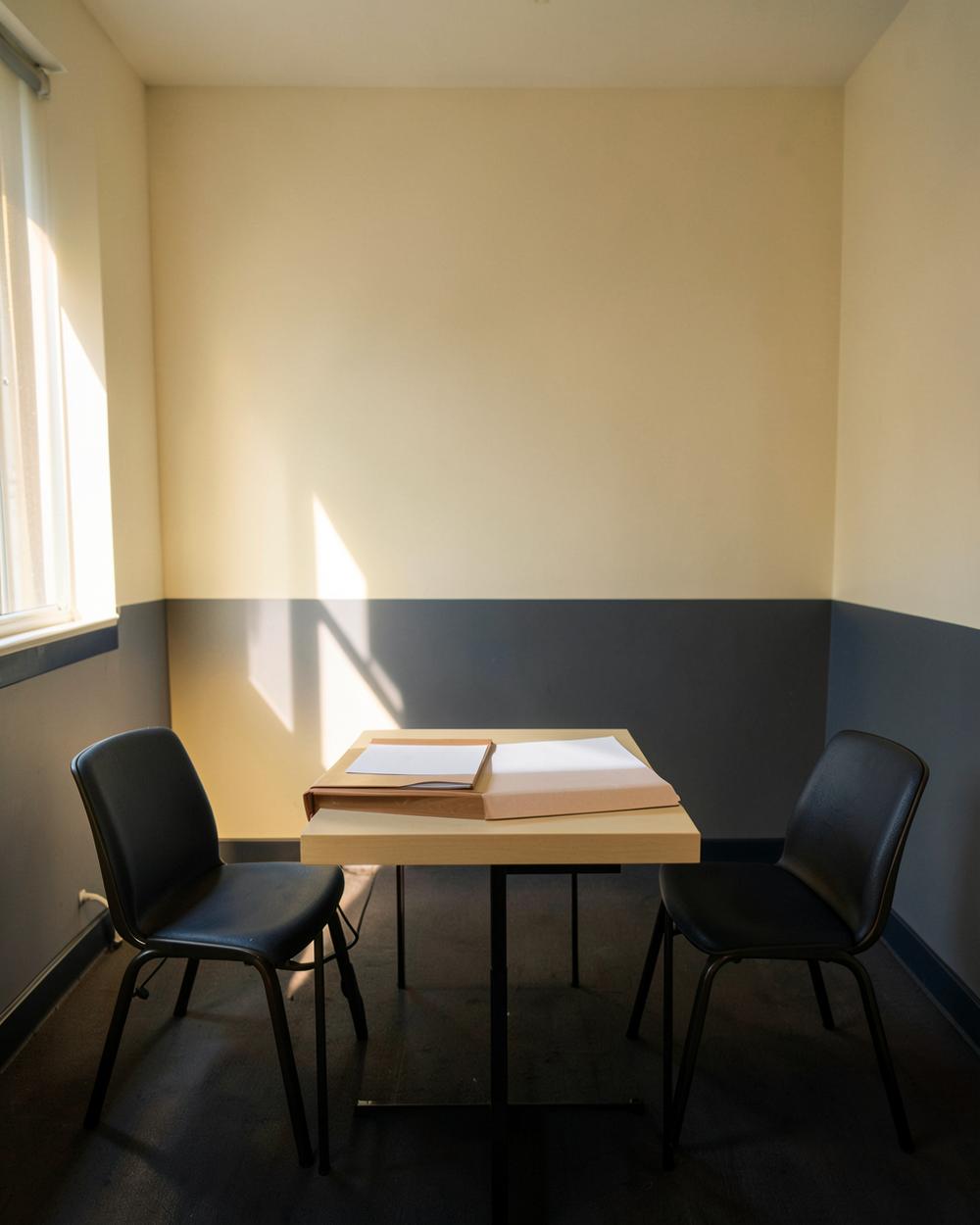 Table ronde et trois chaises vides dans une pièce éclairée par une fenêtre